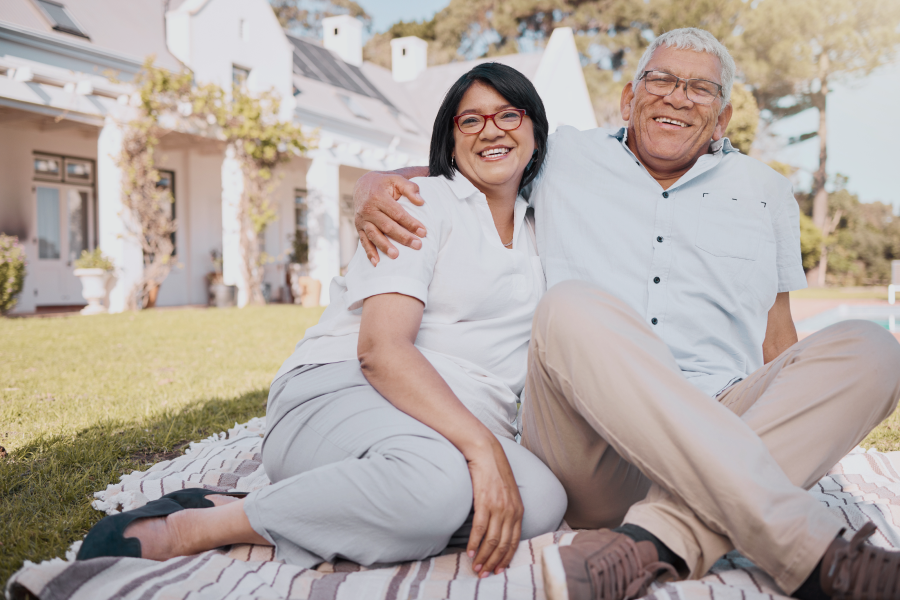 Happy elderly couple standing together in front of their house